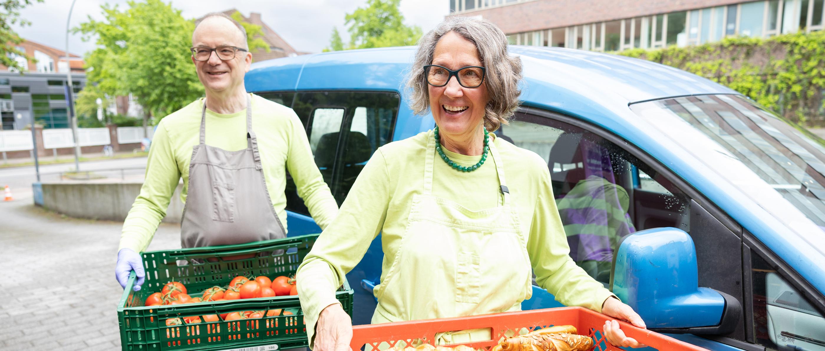 Zwei Ehrenamtliche tragen Kisten mit Essen ins Zentrum für Wohnungslose
