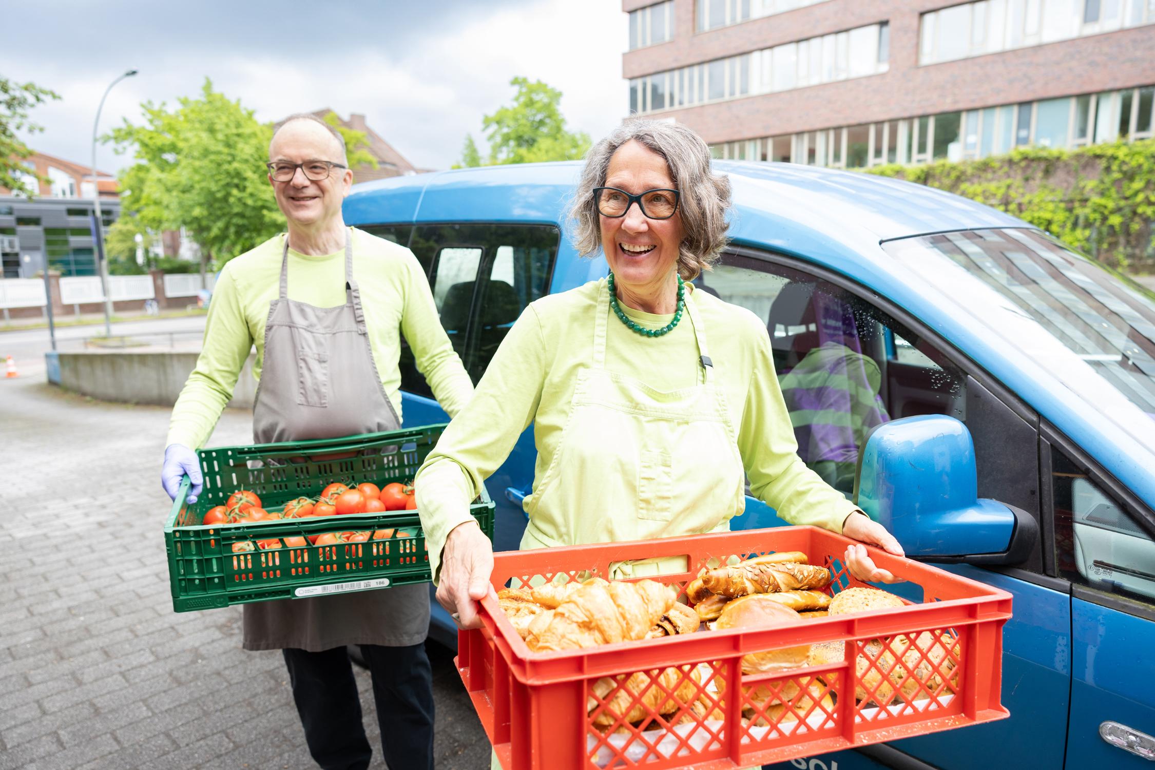 Zwei Ehrenamtliche tragen Kisten mit Essen.