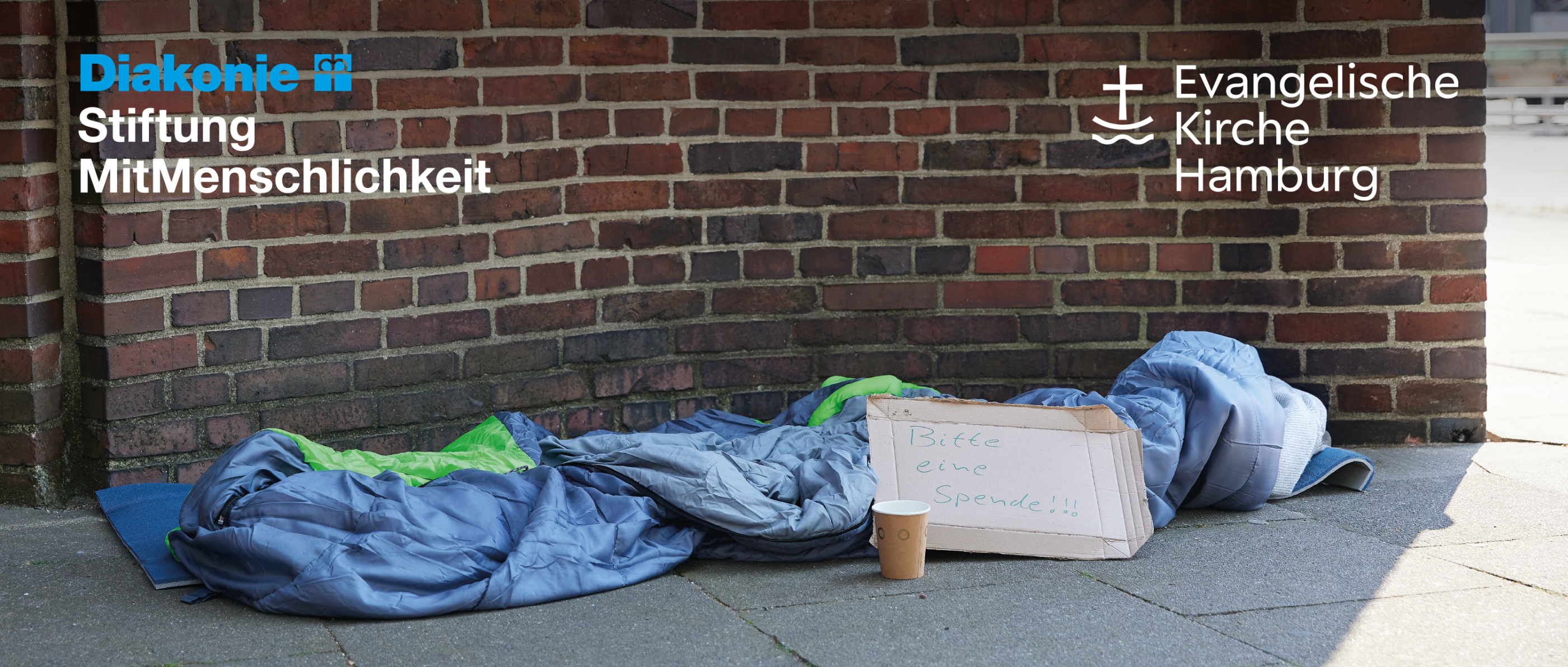 Schlafsack auf dem Boden. Daneben ein Schild: Eine Spende bitte.